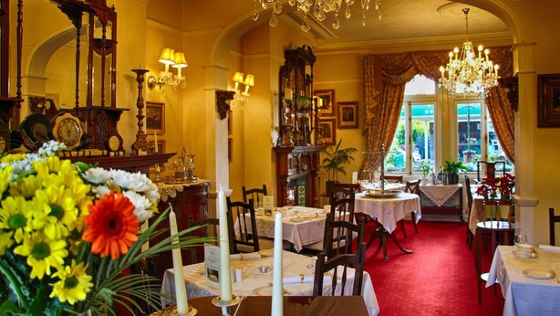 A dining area with chandeliers, tables set for dining, and a red carpet. - Innisfree House (Dundalk)