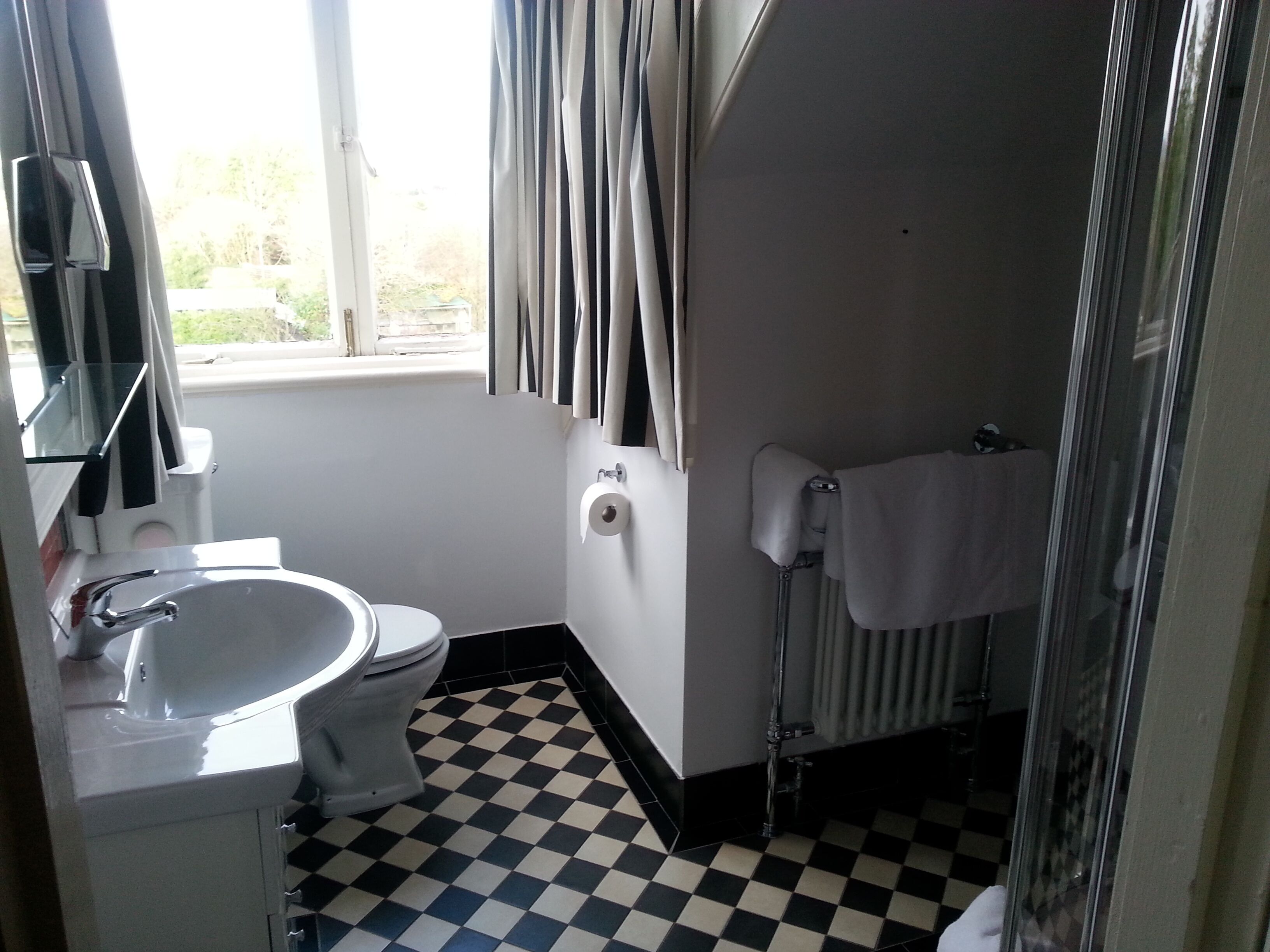 Un baño con piso a cuadros, un lavamanos, un inodoro y un perchero para toallas.