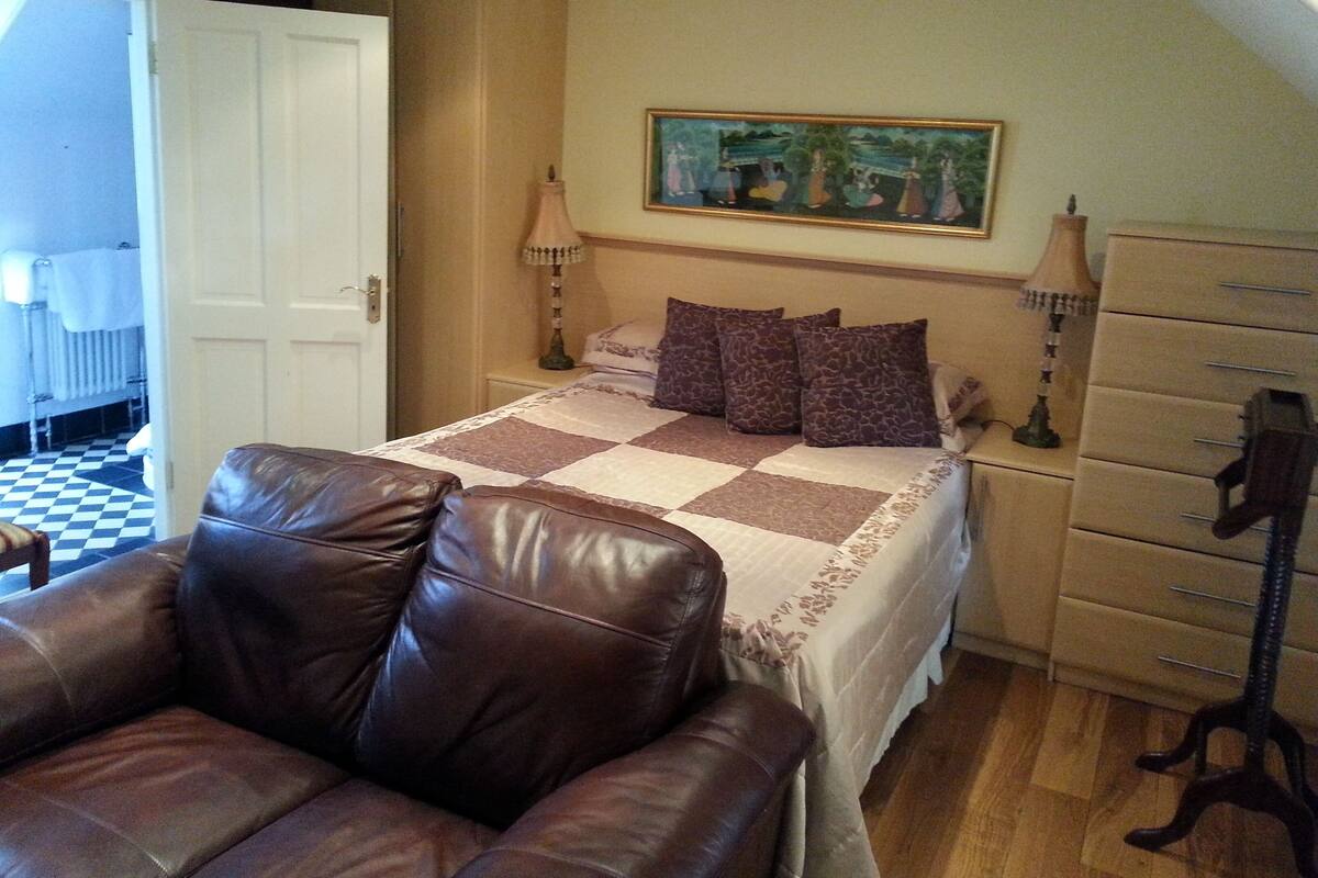 A bedroom with a checkered bedspread, a brown leather chair, a dresser, and a painting on the wall.