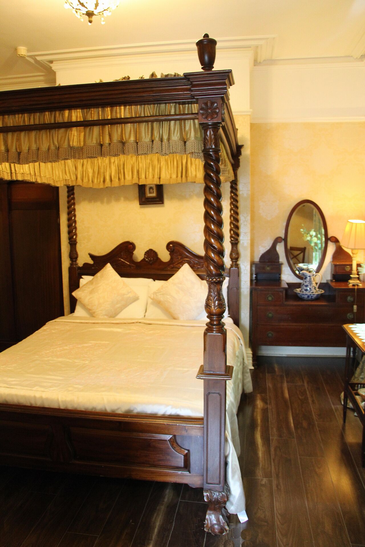 A four-poster bed with a dark wooden frame and a canopy, a wooden dresser with a mirror, and a lamp.