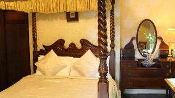 A four-poster bed with a dark wooden frame and a canopy, a wooden dresser with a mirror, and a lamp.