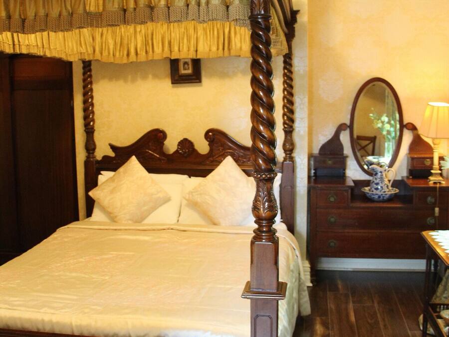 A four-poster bed with a dark wooden frame and a canopy, a wooden dresser with a mirror, and a lamp.