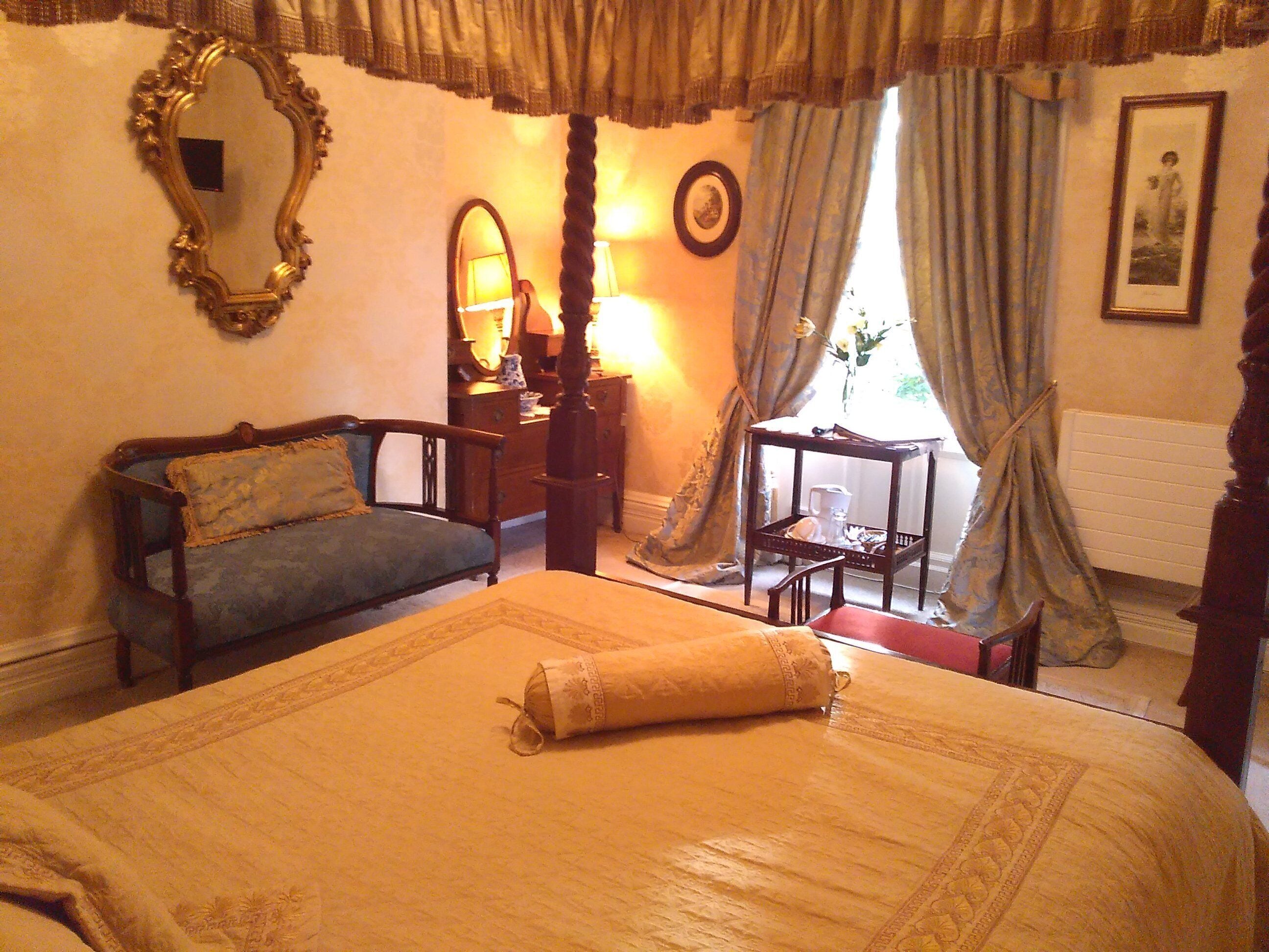 A bedroom with a large bed, a wooden chair, a dresser, a mirror, and a window with curtains.