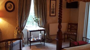 Une chambre à coucher avec un lit à baldaquin, une petite table sur laquelle est posé un vase, une chaise et un radiateur.