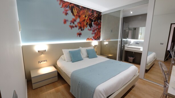A modern bedroom with a large bed, bedside tables, a mirror, and a wall-mounted light fixture. - Hotel Vila da Guarda (A Guarda)