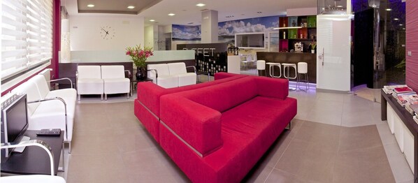 A modern hotel lobby with a red sofa, white chairs, a reception desk, and a bar area. - Hotel Vila da Guarda (A Guarda)