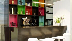 A modern bar area with a dark counter, colorful shelves, and three white bar stools. - Hotel Vila da Guarda (A Guarda)