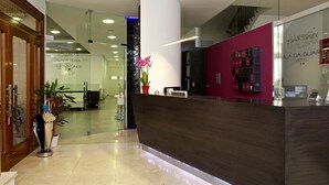 A hotel reception area with a dark reception desk, a glass wall, and a potted plant. - Hotel Vila da Guarda (A Guarda)