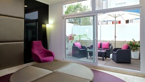 A modern hotel room with a large sliding glass door leading to an outdoor seating area with wicker furniture and potted plants. - Hotel Vila da Guarda (A Guarda)