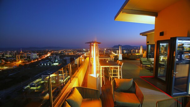 A rooftop terrace with a dining area, seating, and a view of the cityscape at dusk.