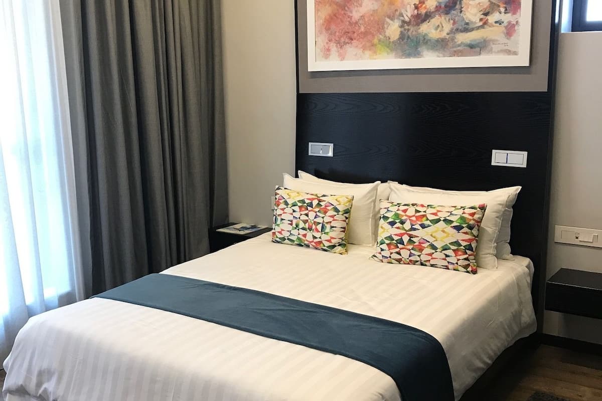 A hotel room with a large bed, a headboard, a painting, and a nightstand.