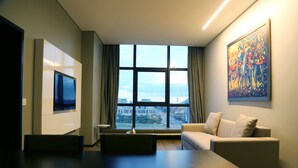 A modern living room with a large window, a flat-screen TV, a sofa, and a colorful painting.