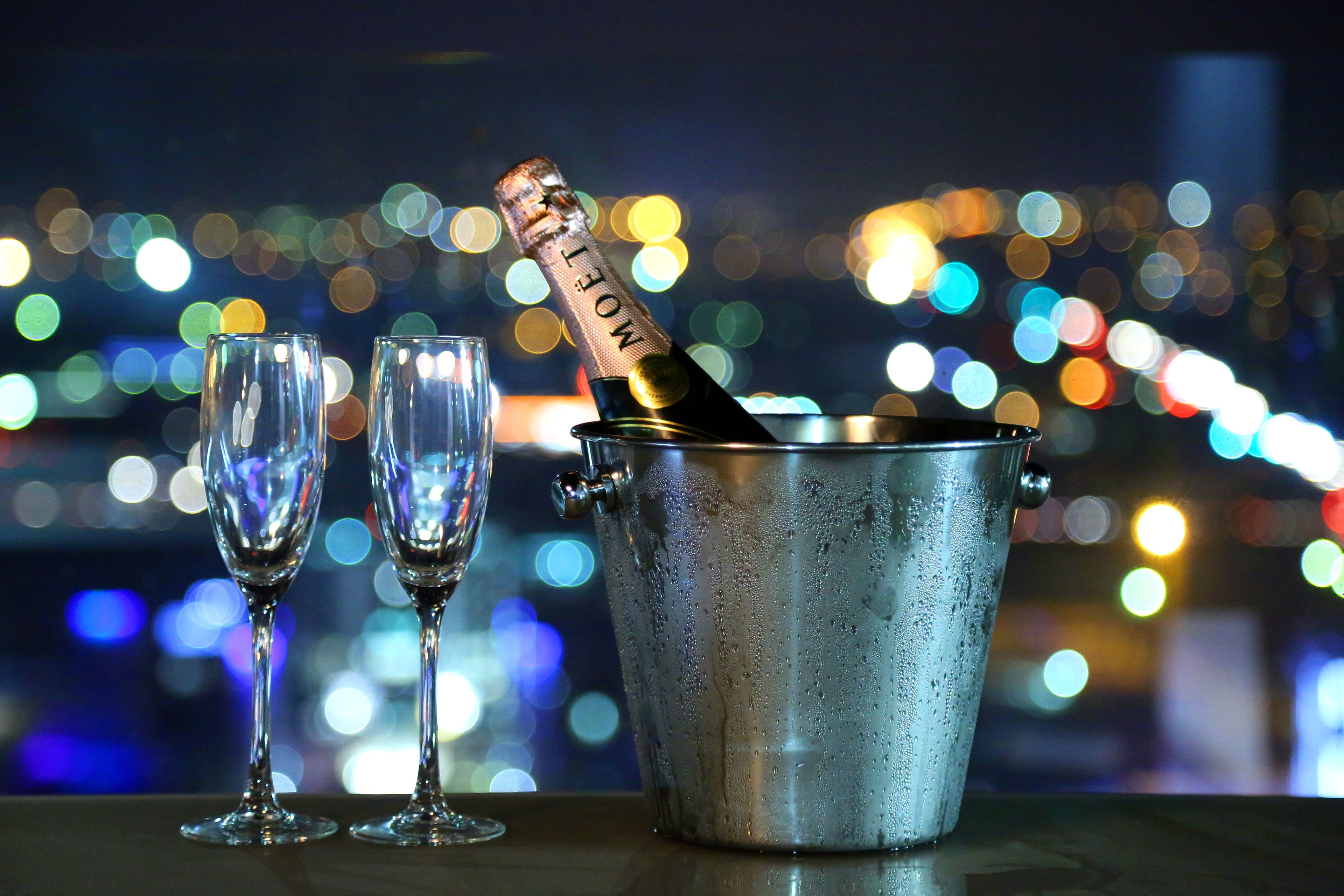 A bottle of champagne in a metal bucket with two empty glasses beside it.
