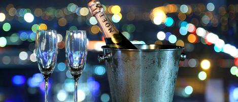 A bottle of champagne in a metal bucket with two empty glasses beside it.