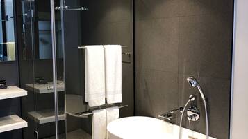 Un baño moderno con una bañera independiente, ducha con mampara de vidrio y tocador con estantes.