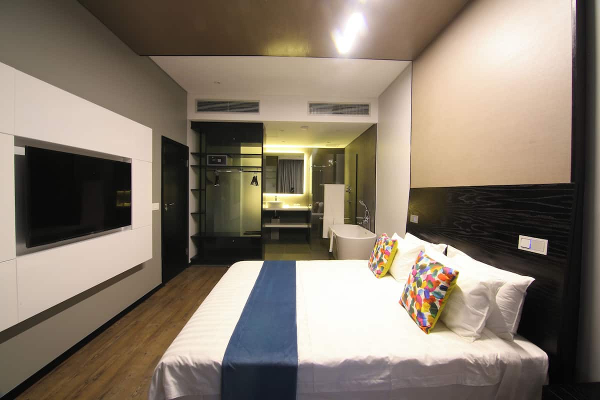 A hotel room with a large bed, a television, a bathroom, and a shower area.