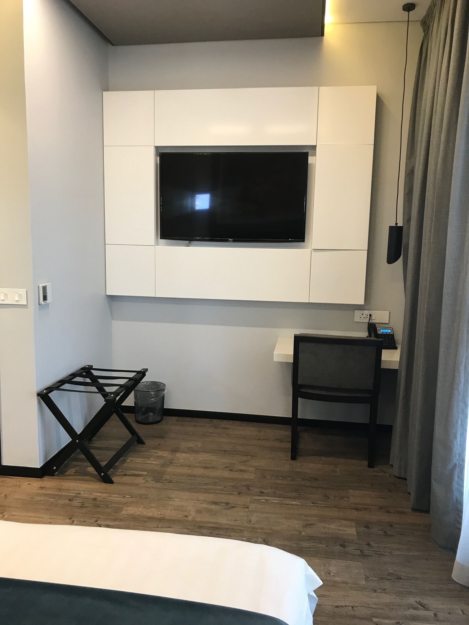 Una habitación de hotel moderna con una televisión de pantalla plana montada en una pared blanca, un escritorio con una silla y una cama con colcha verde.