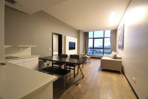 Un apartamento moderno con cocina, comedor y sala de estar. Cuenta con un amplio ventanal con vista a la ciudad, un televisor de pantalla plana y un sofá.