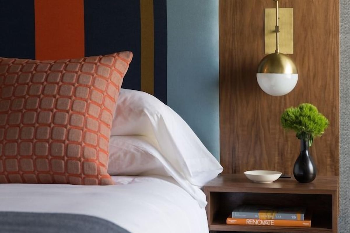 A neatly made bed with a patterned pillow, a bedside table with a lamp, and a small plant.