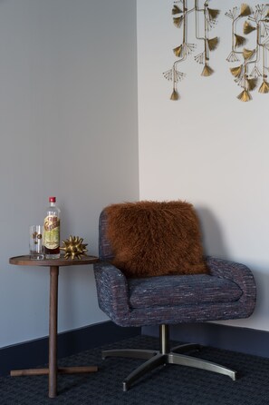 A corner room with a blue armchair, a small round table with a bottle and glass, and a decorative wall hanging. - The Hotel Salem (Salem)