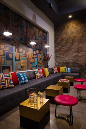 A modern lounge area with a sectional sofa, colorful cushions, a small bar table with drinks, and red stools. - The Hotel Salem (Salem)