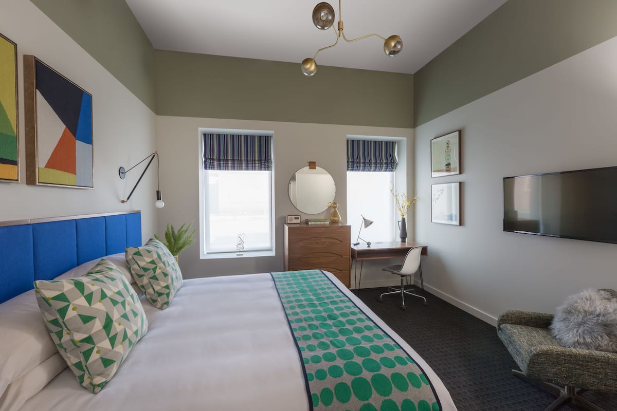 Une chambre d’hôtel avec un grand lit, un bureau, une chaise, une télévision et une fenêtre avec des rideaux.