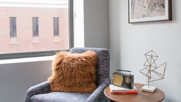 Une pièce moderne avec un fauteuil bleu, une table ronde sur laquelle se trouvent un livre et une horloge, et des tableaux encadrés accrochés au mur.