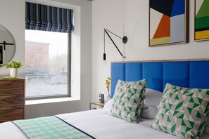 A neatly arranged bedroom with a bed, a bedside table, a dresser, a window with a view, and a wall-mounted lamp. - The Hotel Salem (Salem)