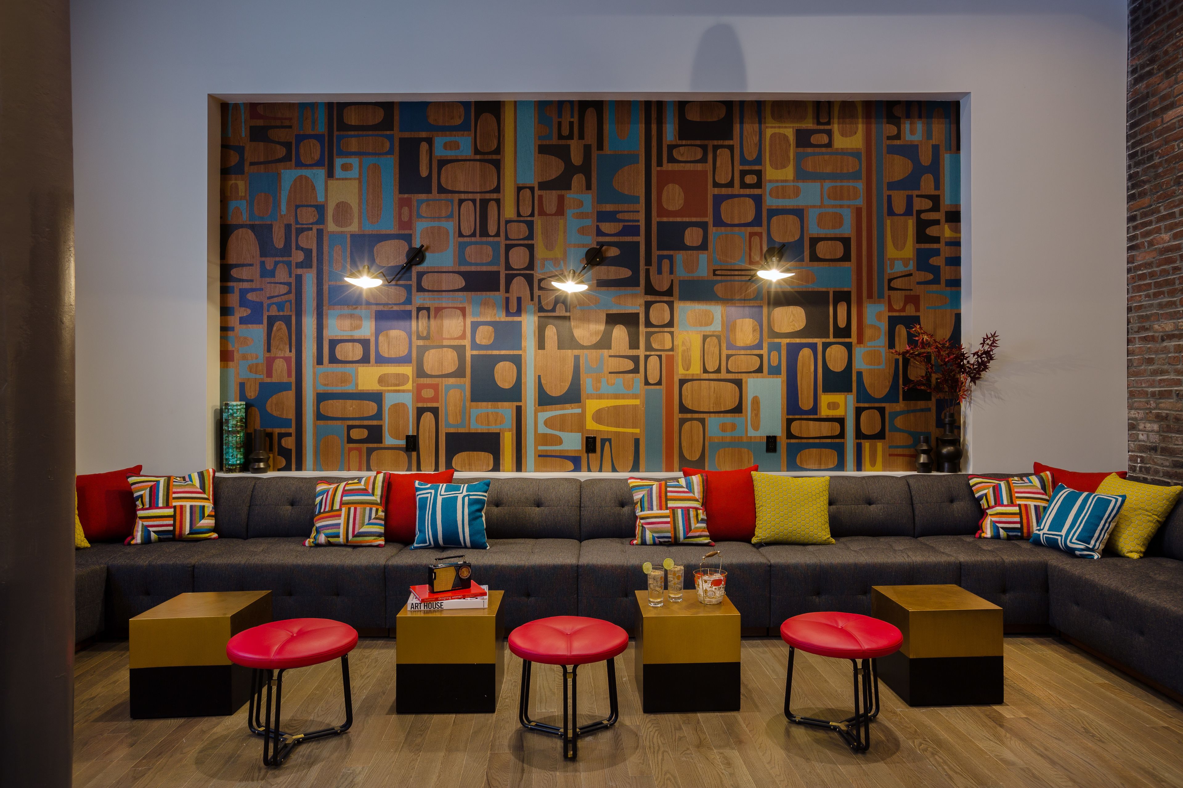 A modern living room with a sectional sofa, red stools, and a colorful abstract wall art.