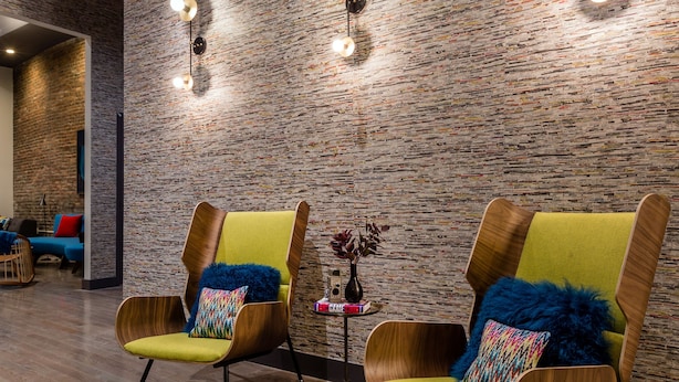 A modern interior with two wooden armchairs with yellow cushions, a brick-patterned wall, and wall-mounted lighting. - The Hotel Salem (Salem)
