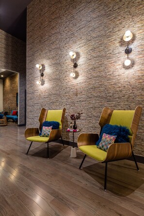 A modern interior with two wooden armchairs with yellow cushions, a brick-patterned wall, and wall-mounted lighting. - The Hotel Salem (Salem)