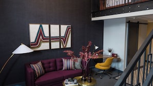 A modern living room with a dark wall, a purple sofa, a yellow armchair, and a chandelier. - The Hotel Salem (Salem)