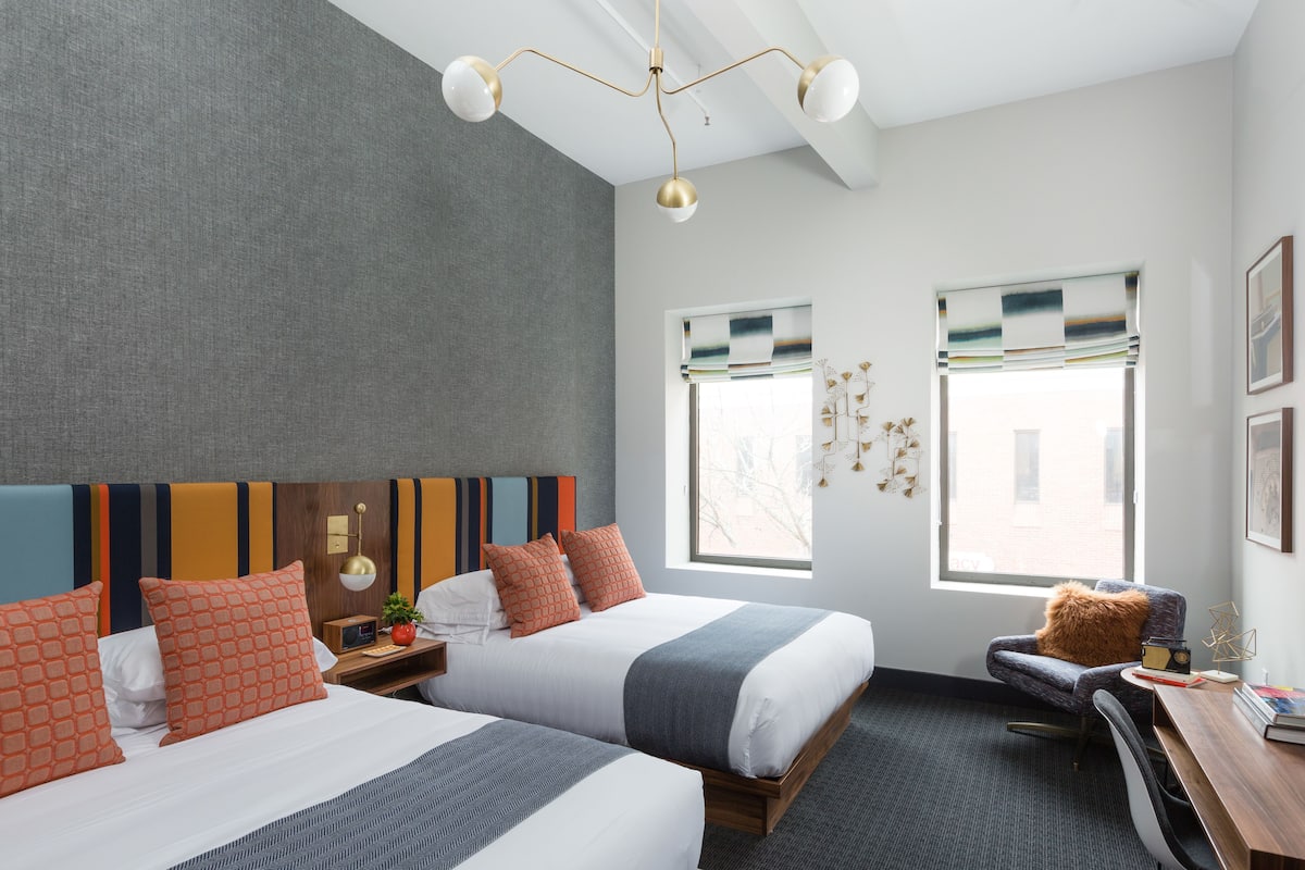 Une chambre d’hôtel moderne avec deux lits, un bureau et une chaise.