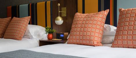 Habitación de hotel con cama, dos almohadas, mesita de noche con radio, planta y pared con papel tapiz a rayas.