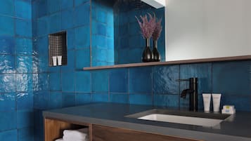 A bathroom with a blue tiled wall, a wooden vanity, a sink, and two vases with purple flowers.
