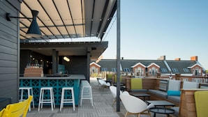 An outdoor seating area with wooden tables and chairs, a bar counter, and a view of residential buildings in the background. - The Hotel Salem (Salem)