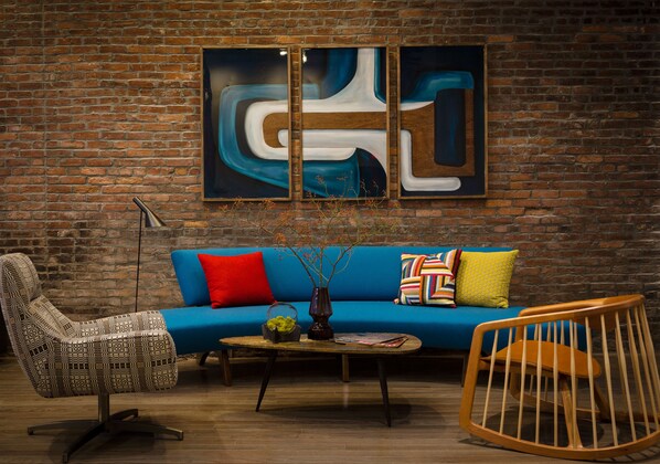 A room with a brick wall, a blue sofa with colorful cushions, a patterned armchair, a wooden rocking chair, and a coffee table with a vase and books. - The Hotel Salem (Salem)