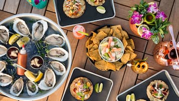 A variety of seafood dishes, including oysters on the half shell, tacos, and a shrimp cocktail, arranged on a wooden table.