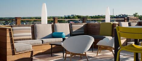 A rooftop terrace with a wooden deck, a sofa set, and a yellow chair.