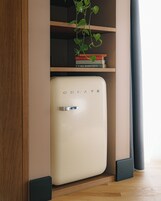 A white mini-fridge with the word "CREATE" on it, placed in a wooden cabinet with a plant on top.