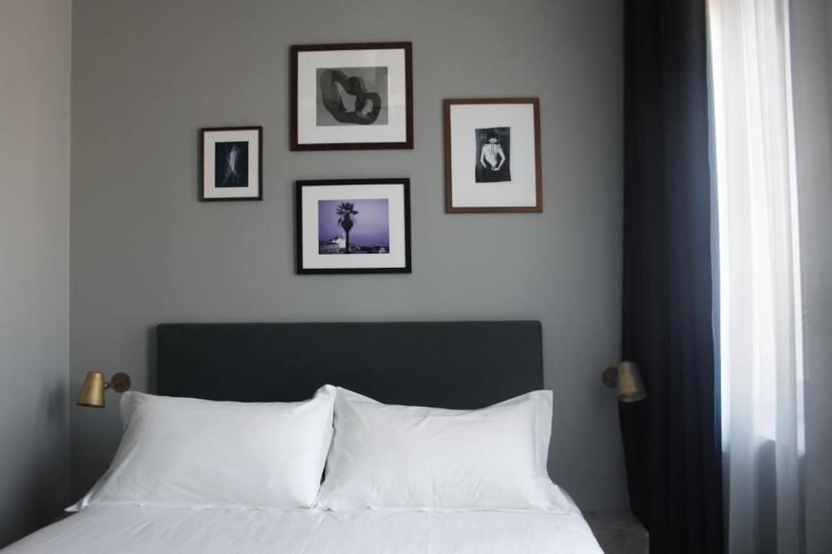 A hotel room with a bed, framed pictures on the wall, and two bedside lamps.
