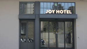The exterior of Joy Hotel with a large glass entrance, a sign above the doors, and a reflection of a motorbike in the window. - c-hotels Joy (Florence)