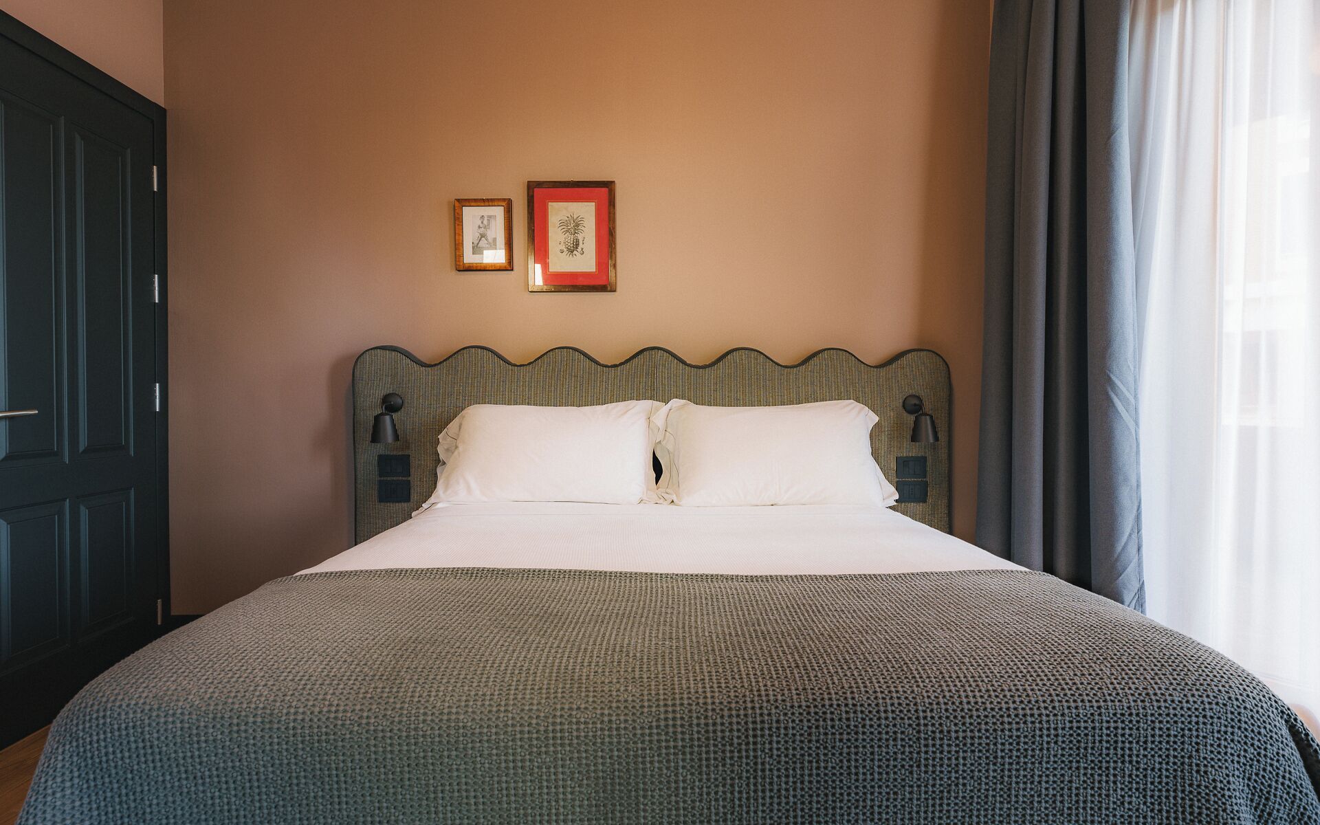 A neatly made bed with a patterned bedspread, a wavy headboard, and two framed pictures on the wall.