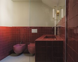 Casa de banho com azulejos vermelhos, um bidé assentado, uma sanita e uma pia retangular.