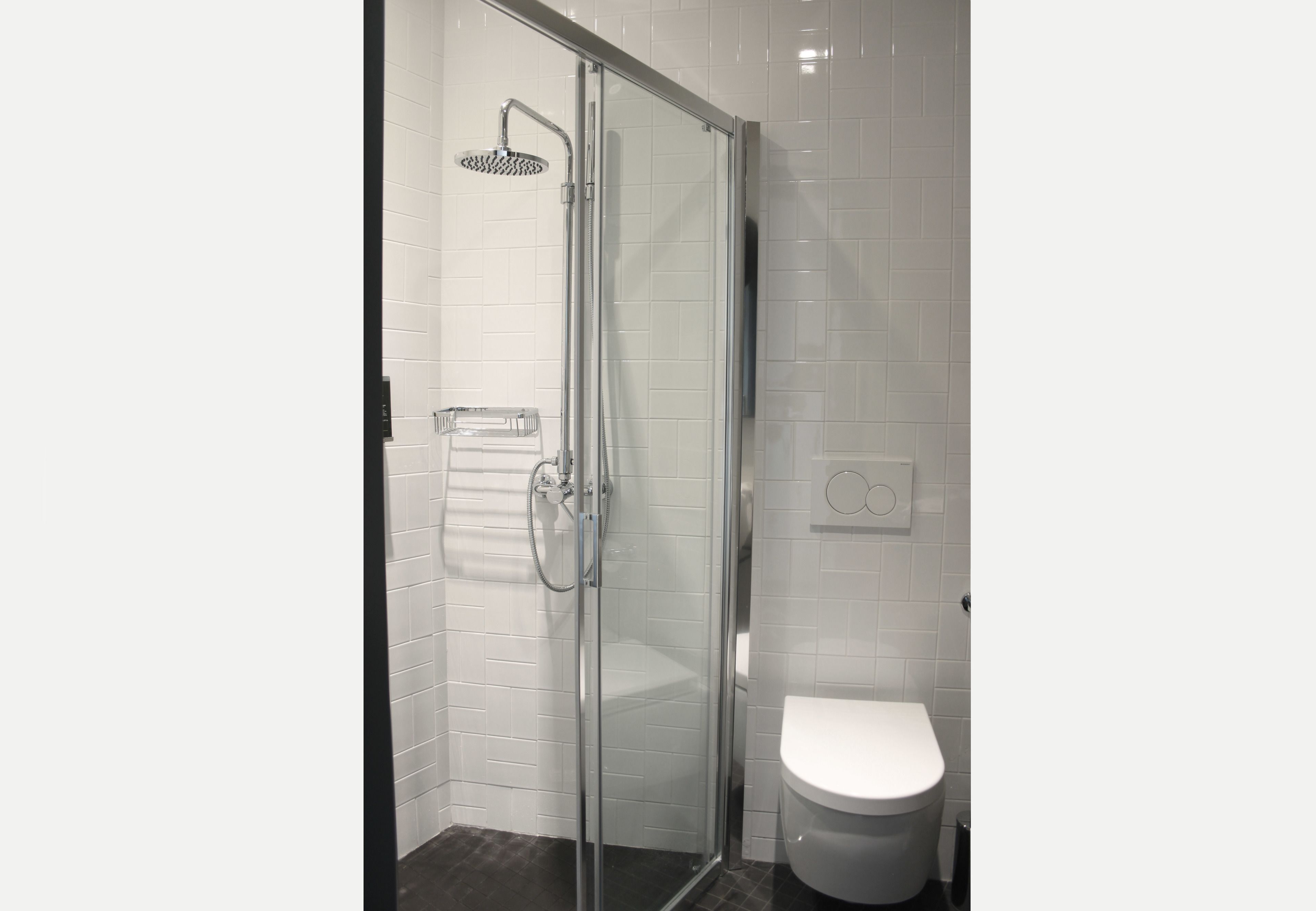 Une salle de bain moderne avec une douche à l’italienne en verre, des toilettes blanches et un mur carrelé.