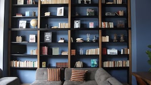 A room with a large bookshelf filled with books and decorative items, a grey sofa with patterned cushions, and a chandelier. - c-hotels Joy (Florence)