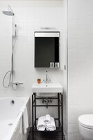 Un baño moderno con una bañera blanca, un lavamanos con un espejo encima y un cabezal de ducha.