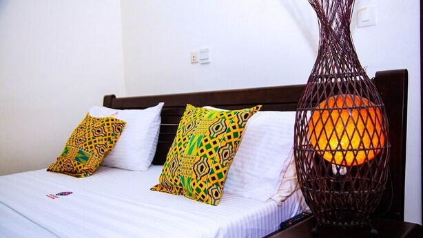 A bed with white linens, two patterned pillows, and a decorative metal lamp. - Cypa Hotel (Abidjan)