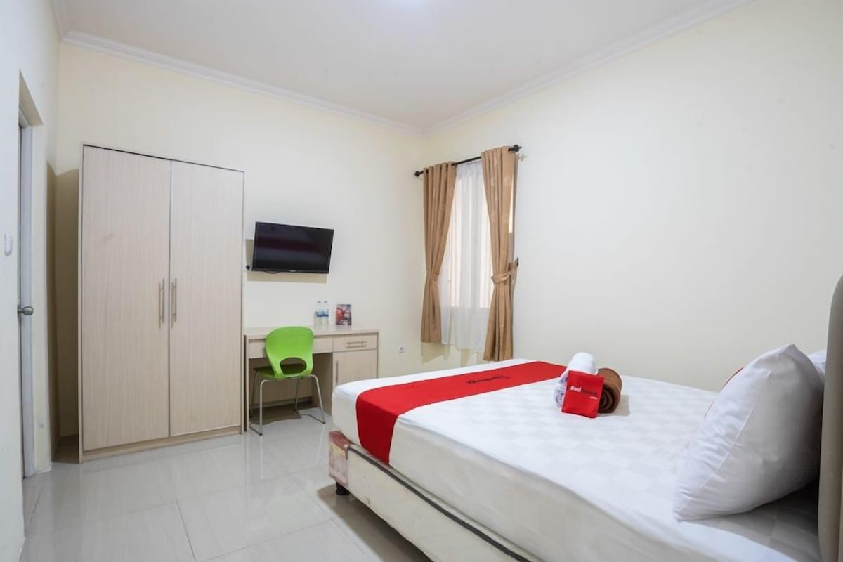 A hotel room with a bed, a desk, a chair, a wardrobe, and a TV.