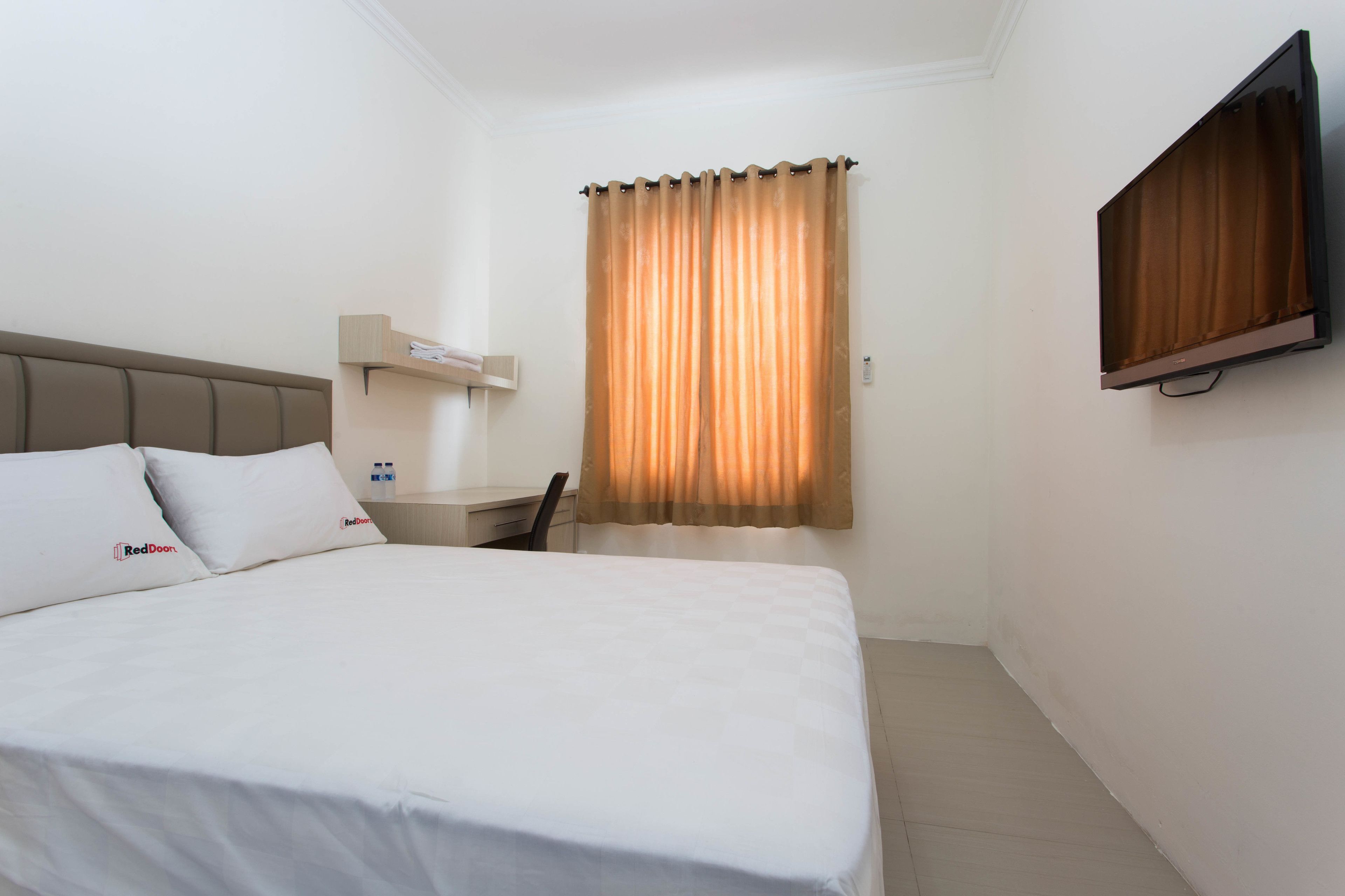 A hotel room with a bed, a desk, a chair, a TV, and a window with curtains.